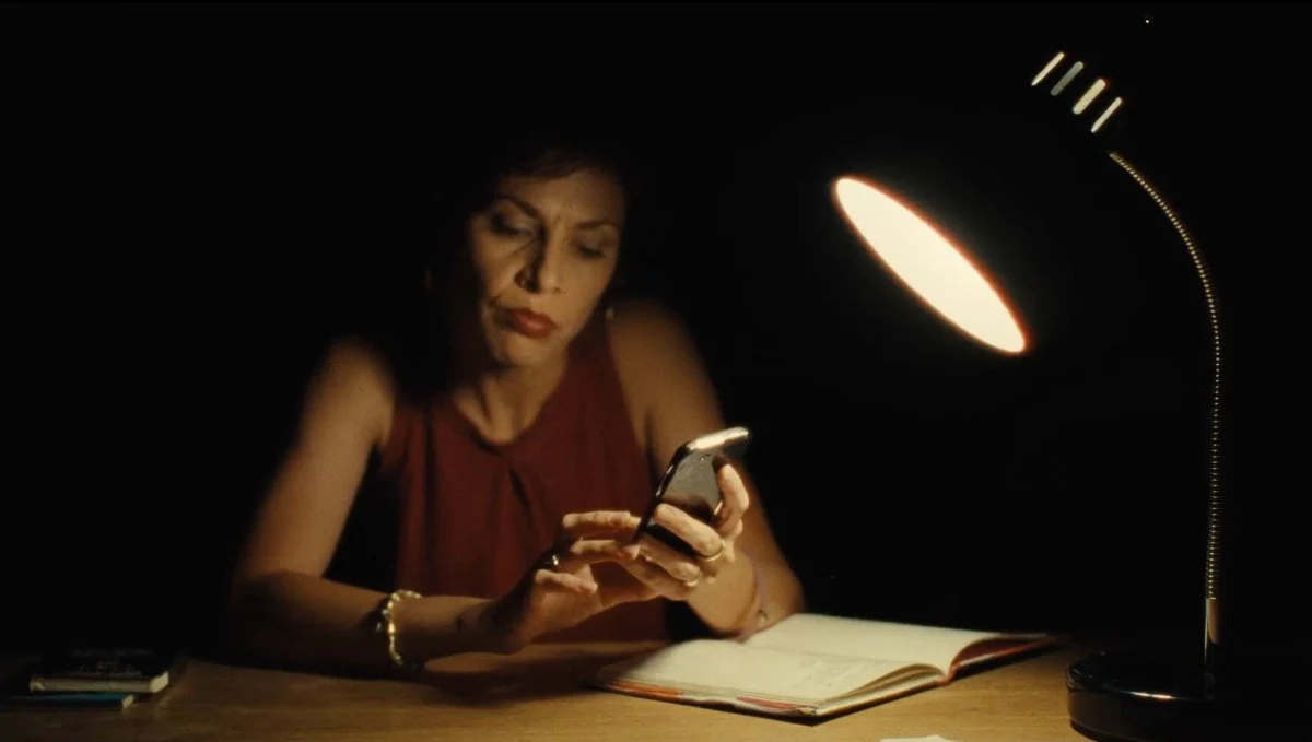 Una mujer ante una lámpara encendida, con una libreta abierta al lado, revisando mensajes en el móvil para comprobar su memoria